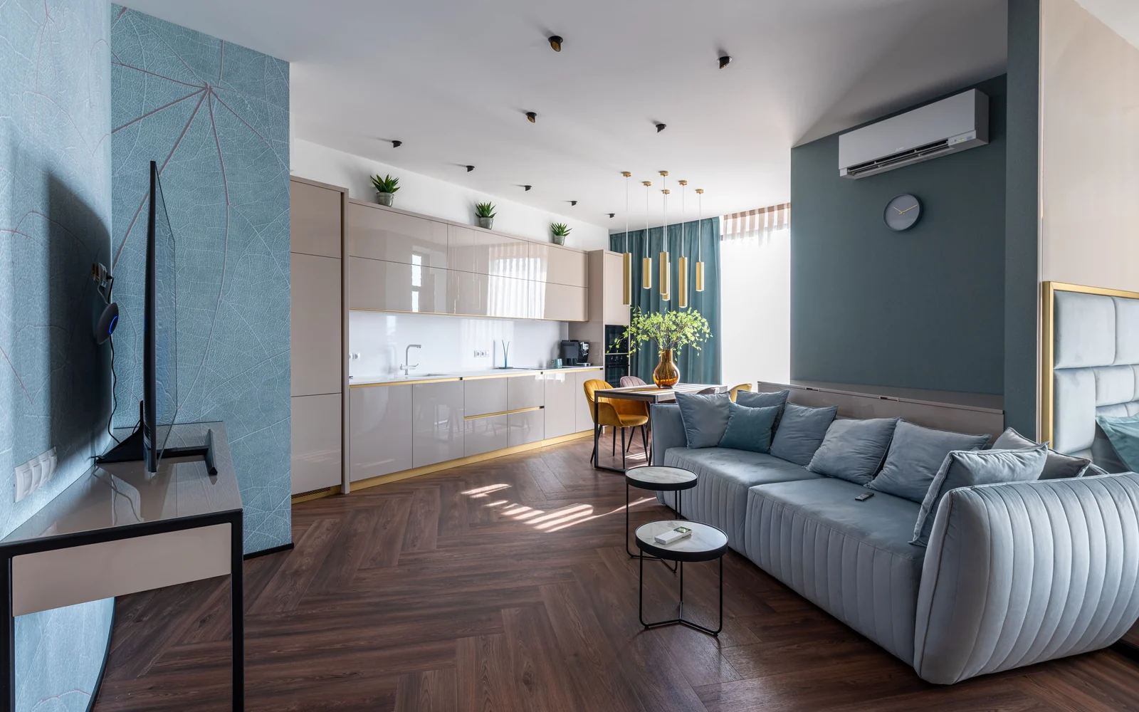 Wall-mounted air conditioner in a sunlit living room with a teal sofa and wooden flooring